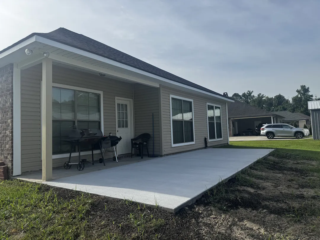 Covered back patio and an open concrete slab on a tan-siding home before a screen room was built, from a Tiger Town Construction project