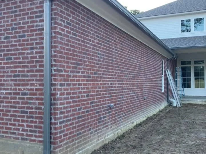 Bronze seamless gutter and downspout running along a brick home wall, by Tiger Town Construction