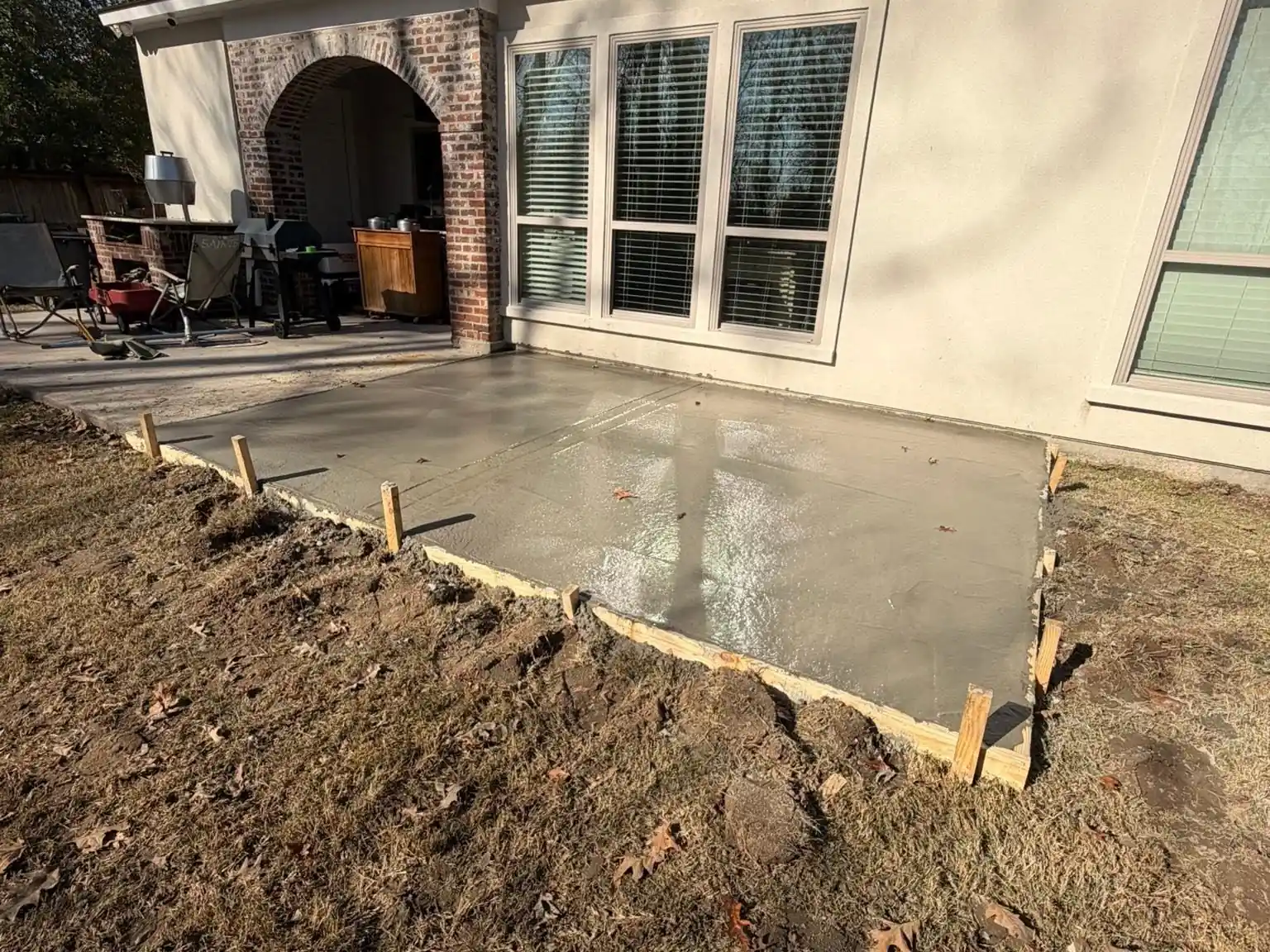 Freshly poured concrete patio slab with wood forms still set along the edge at a brick home, by Tiger Town Construction