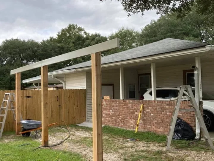 Cedar posts and a white beam set in place during framing beside a brick home, with ladders on site, on a Tiger Town Construction job